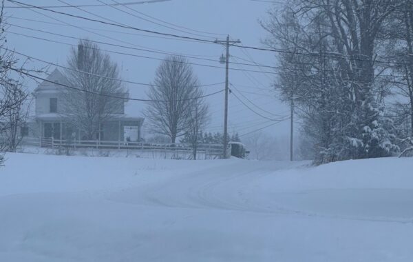Evergreen Life Services - Winter Storm 2026. Photo is a farm house with a white fence. The roads are covered in snow and ice. The sky is gray and hazy.