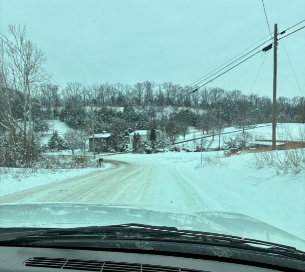 Evergreen Life Services - Winter Storm 2026. Photo from truck of road conditions in TN. Roard are covered in snow and ice. The vehicle is approaching some homes and buildings. 