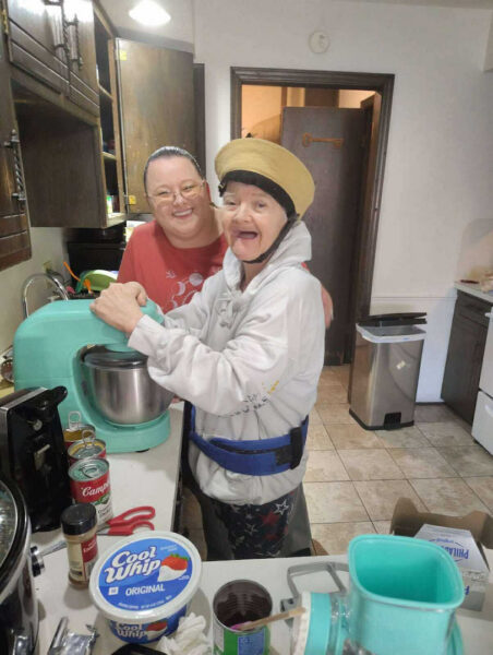 Evergreen Community Home in Oklahoma. Individual served by Evergreen is involved in cooking a meal with support staff. They are in front of the kitchen stand mixer and ingredients for casserole and desserts are out for meal preparation.